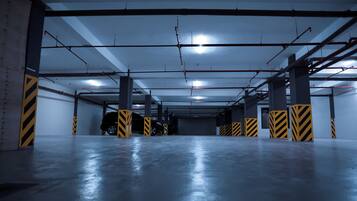 Un parking à plusieurs niveaux, doté de planchers en béton, de barrières rayées de jaune et de noir, et de poutres apparentes.