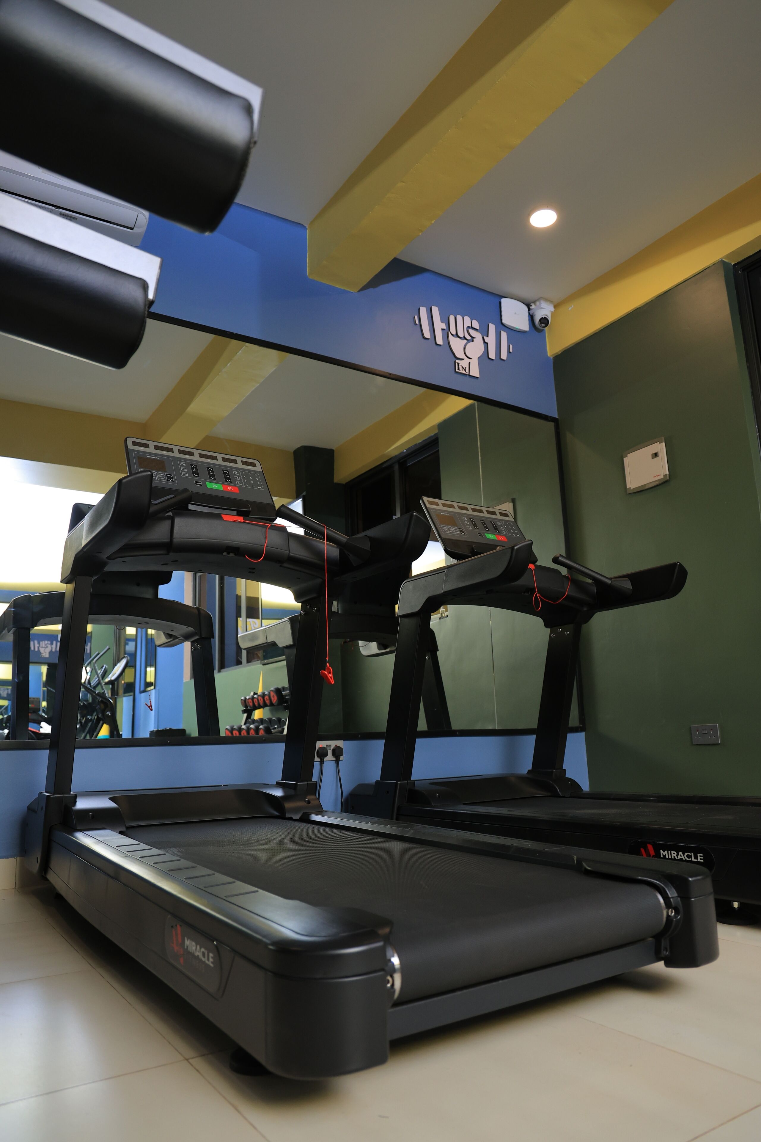 A treadmill in a gym with a control panel, a mirrored wall, and exercise equipment in the background.