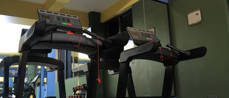 A treadmill in a gym with a control panel, a mirrored wall, and exercise equipment in the background.