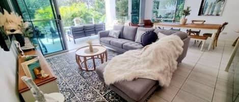 A modern living room with a grey sofa, a white furry throw, and a dining area with a wooden table and chairs.