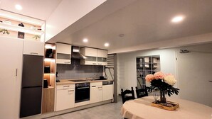A modern kitchen with built-in appliances, a dining area with a table and chairs, and a small potted plant on the table. - MoselVilla No7 Deluxe Apartment (Pommern)