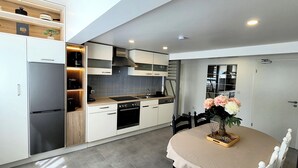 A modern kitchen with white cabinets, a built-in oven, and a dining area with a table and chairs. - MoselVilla No7 Deluxe Apartment (Pommern)