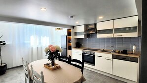 A modern kitchen with white cabinets, a built-in oven, and a sink. There is a dining table with chairs and a vase of flowers. - MoselVilla No7 Deluxe Apartment (Pommern)