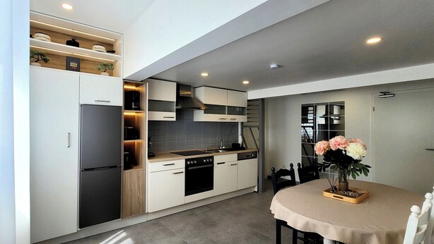 A modern kitchen with built-in appliances, a dining area with a table and chairs, and a staircase leading to another level. - MoselVilla No7 Deluxe Apartment (Pommern)