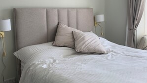 A neatly made bed with a headboard, two bedside lamps, and a window with curtains.
