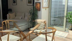 A modern living room with a glass door leading to a balcony, wooden chairs, a sofa, and framed artwork on the walls.