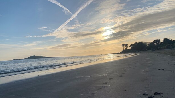 A beach with footprints leading towards the water, a clear sky, and a distant landmass.