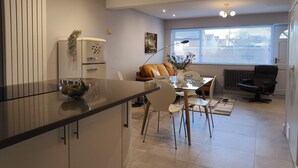 Una cocina moderna con una isla central, un área de comedor con mesa y sillas, una silla de oficina negra y una ventana con persianas.