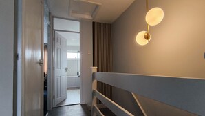 Un pasillo con una escalera, una puerta que da a otra habitación y una lámpara fijada a la pared.
