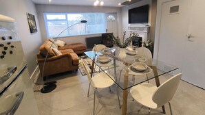 Una sala de estar moderna con una mesa de comedor de cristal, sillas blancas, un sofá marrón y una chimenea.
