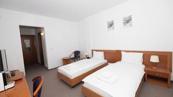 Et hotelværelse med to senge, et skrivebord med stol, et lille bord og et natbord med lampe.