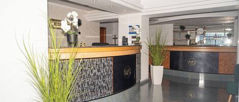 A hotel reception area with a curved reception desk, potted plants, and a modern interior design.