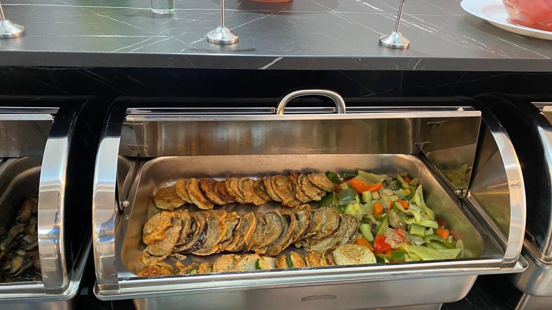 Un bufé con diversos alimentos, incluyendo opciones fritas y una ensalada de verduras.