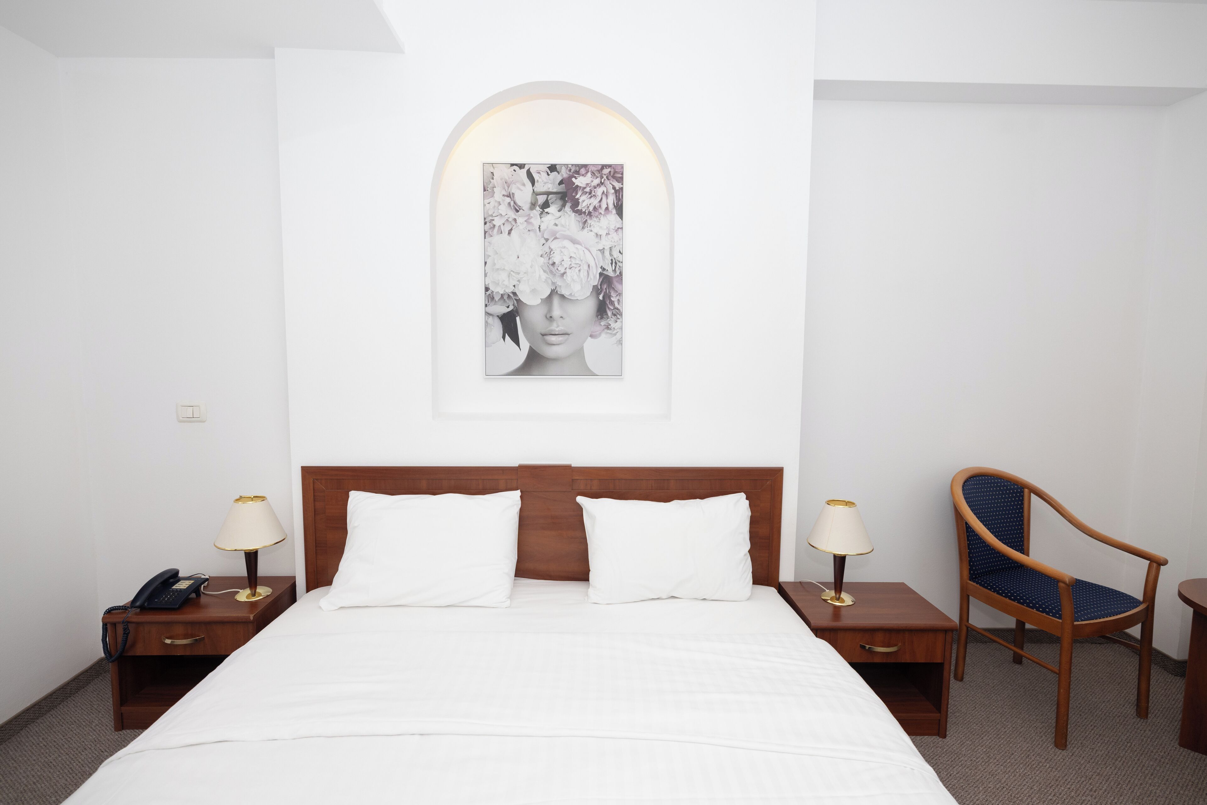 Una habitación de hotel con una cama, dos mesitas de noche, una silla y un cuadro colgado en la pared.