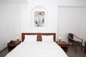 Una habitación de hotel con una cama, dos mesitas de noche, una silla y un cuadro colgado en la pared.