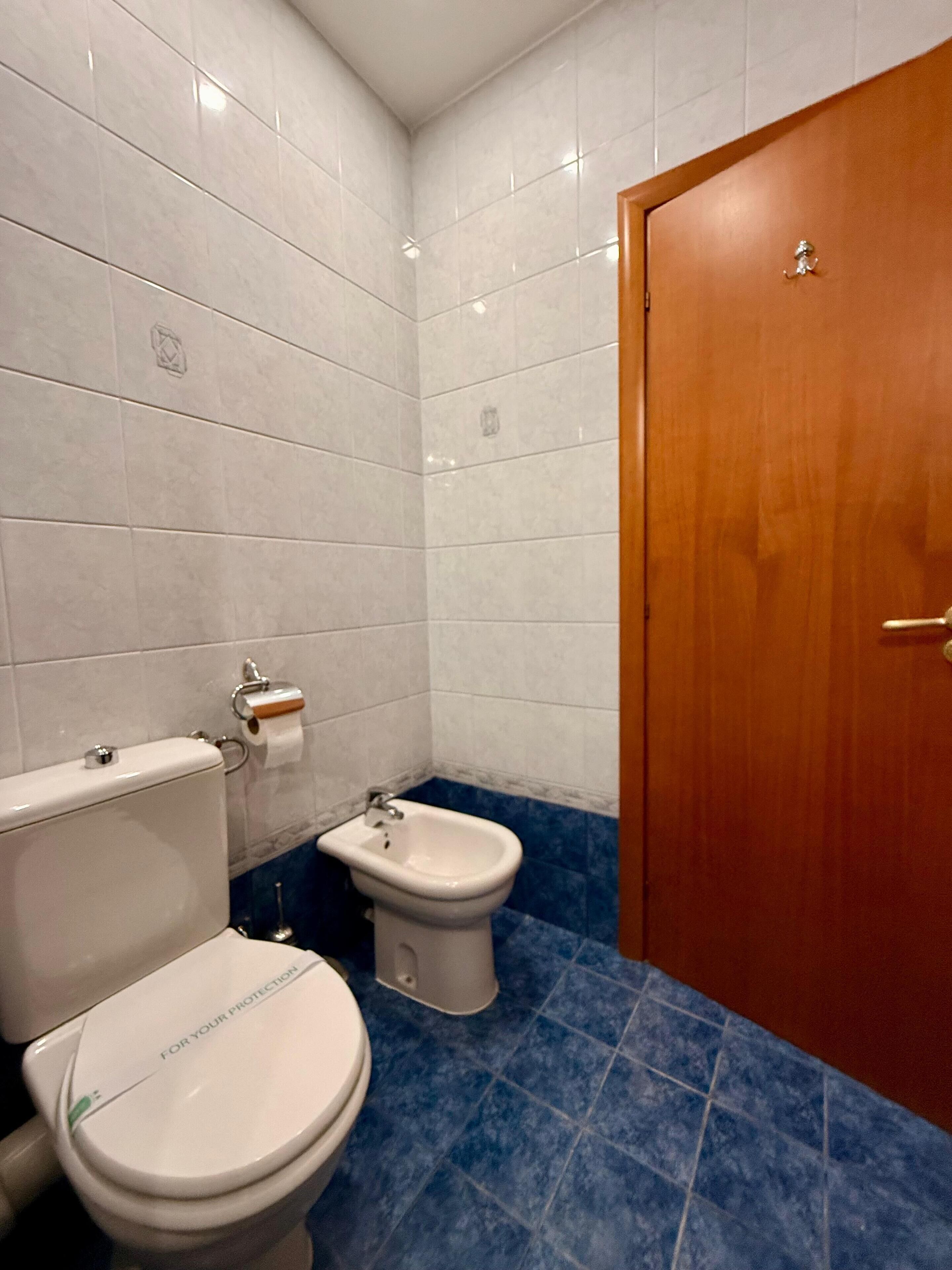 A bathroom with a toilet, bidet, and a wooden door.