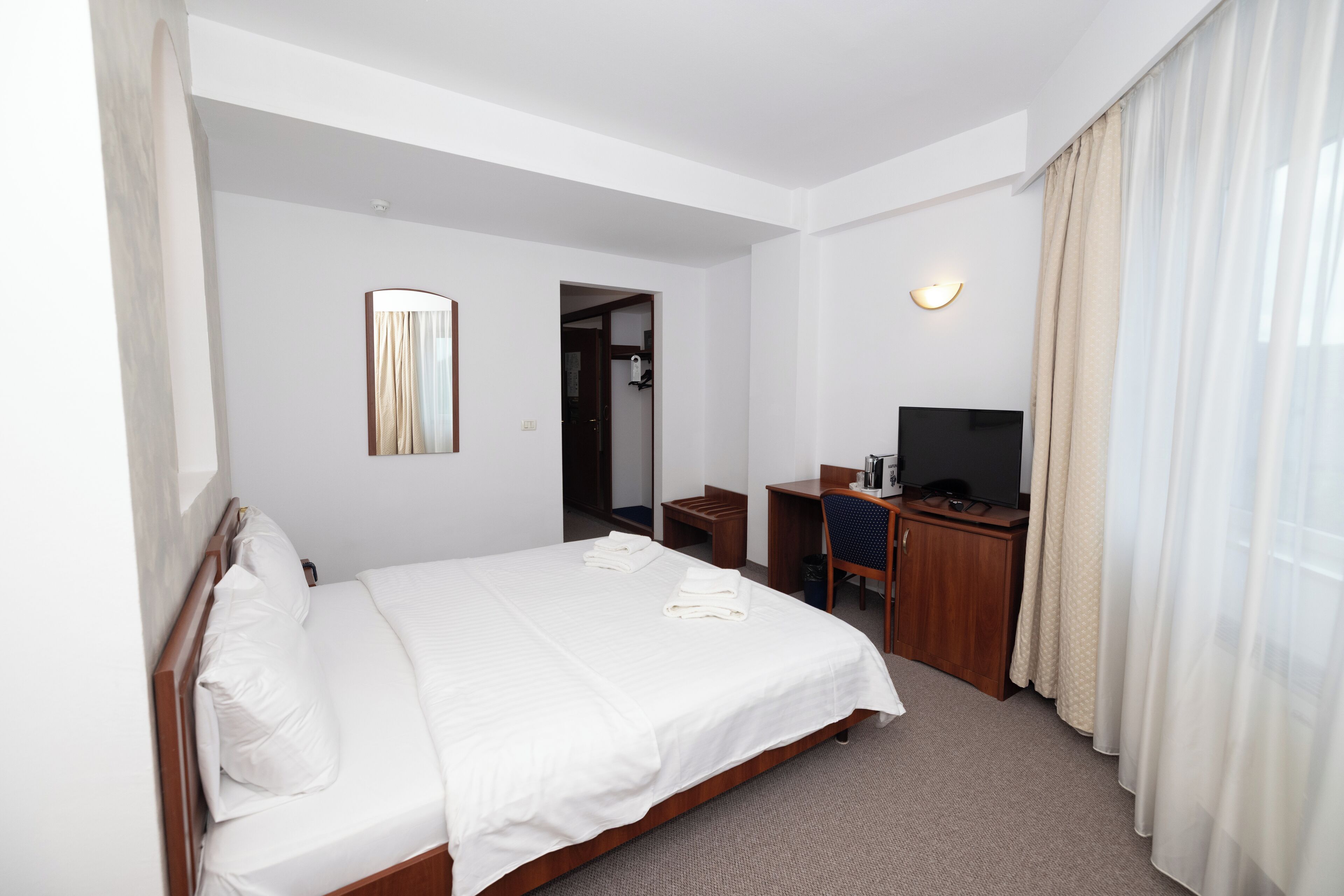 A hotel room with a bed, a desk, a chair, a television, and a mirror.