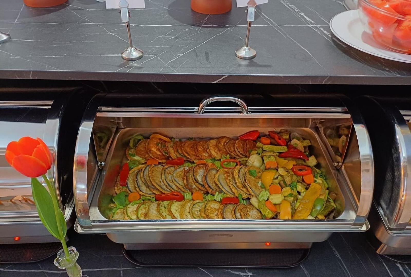 Un bufé con papas en rodajas, verduras mixtas y una tulipán roja.