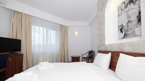 A hotel room with a large bed, a television, a chair, and a small table. - Hotel Excelsior (Timisoara)