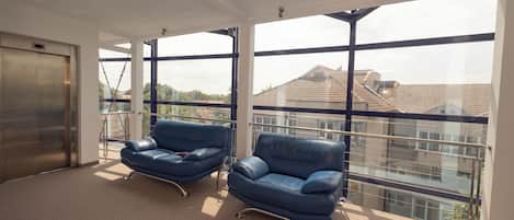A spacious room with large windows, two blue leather chairs, a carpeted floor, and a visible elevator.