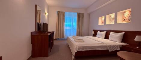 Une chambre d’hôtel avec un lit, un bureau, une chaise, une télévision et une fenêtre avec des rideaux.