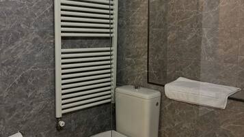 Un baño con inodoro, toallero, cesto de basura y zona de ducha.