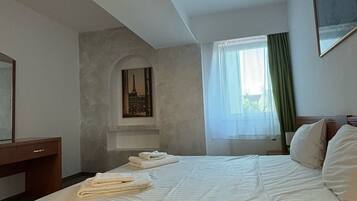 A hotel room with a large bed, a desk, a chair, a window with curtains, and a painting of the Eiffel Tower.
