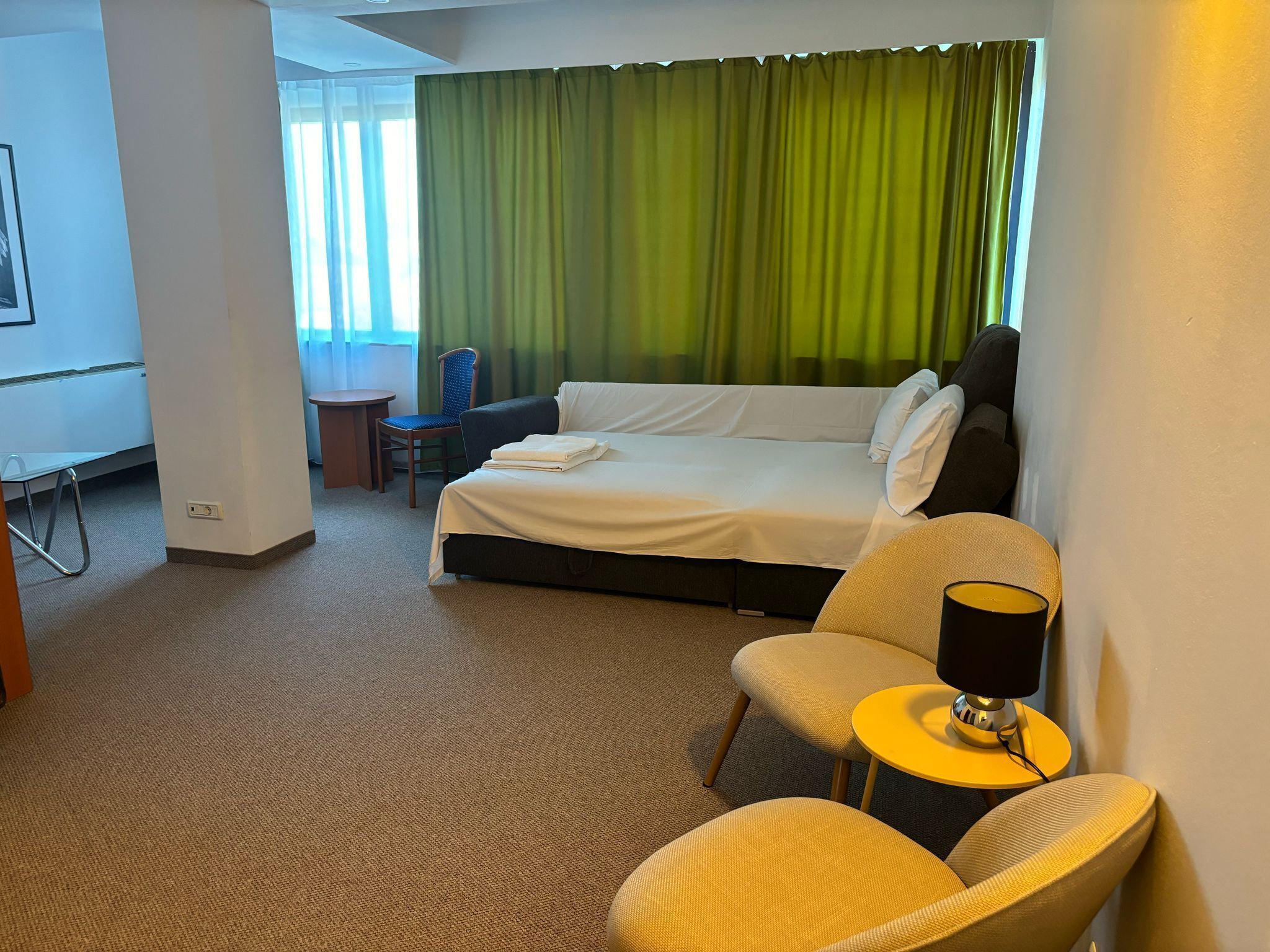 A hotel room with a bed, a chair, a small table, and a desk.