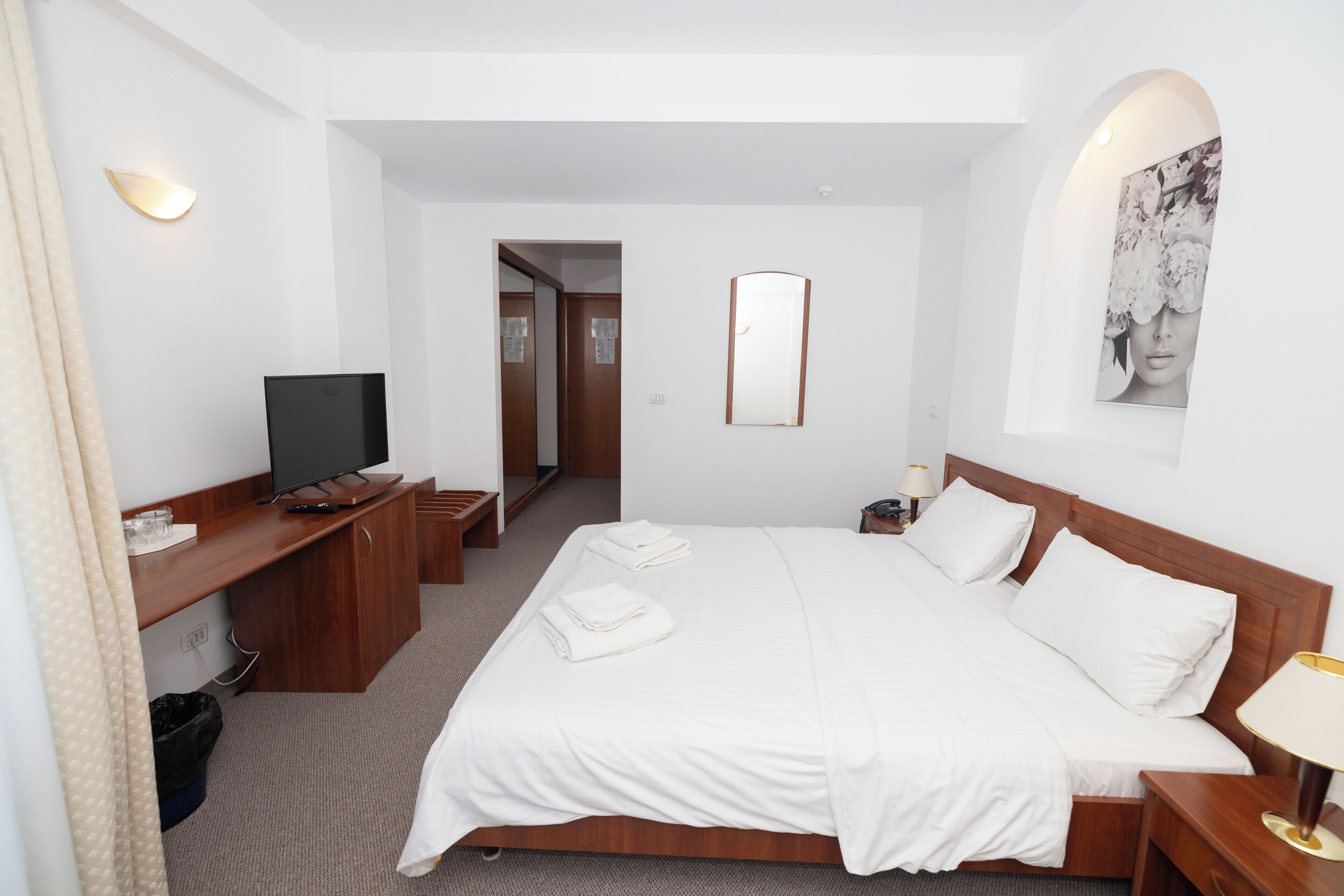 Habitación de hotel con cama, escritorio con televisor, espejo y un cuadro en la pared.