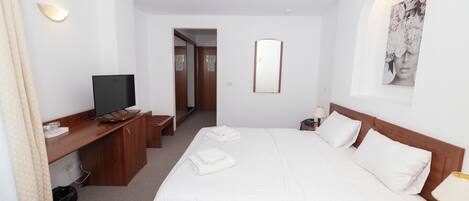 Habitación de hotel con cama, escritorio con televisor, espejo y un cuadro en la pared.