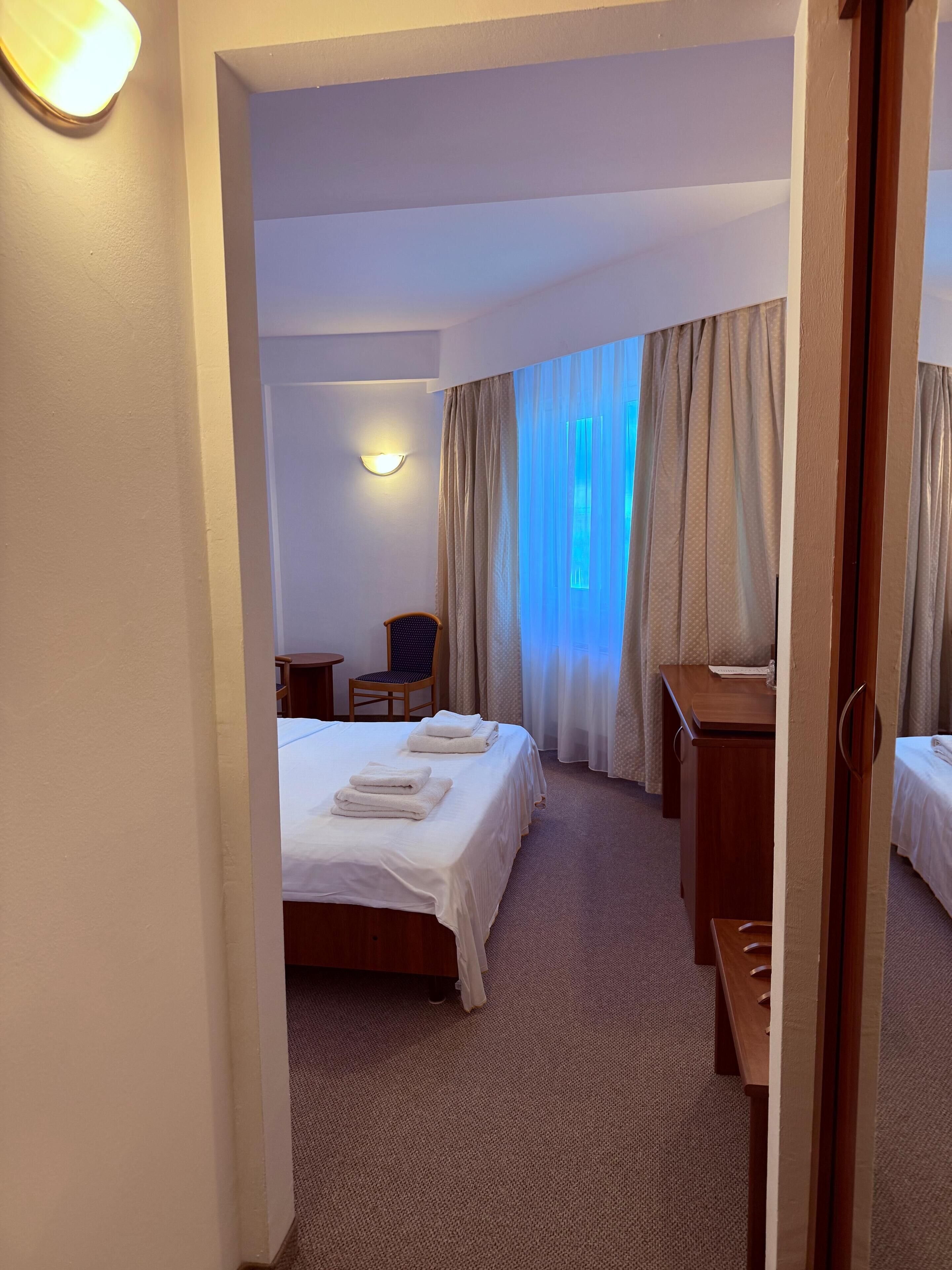 Una habitación de hotel con cama, escritorio, silla y ventana con cortinas.