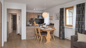 A modern kitchen with wooden cabinets, a dining table with chairs, a hanging light fixture, and a window with curtains. - Nice apartment for 4 people with WIFI, pool, TV, balcony, pets allowed and panoramic view (Falera)