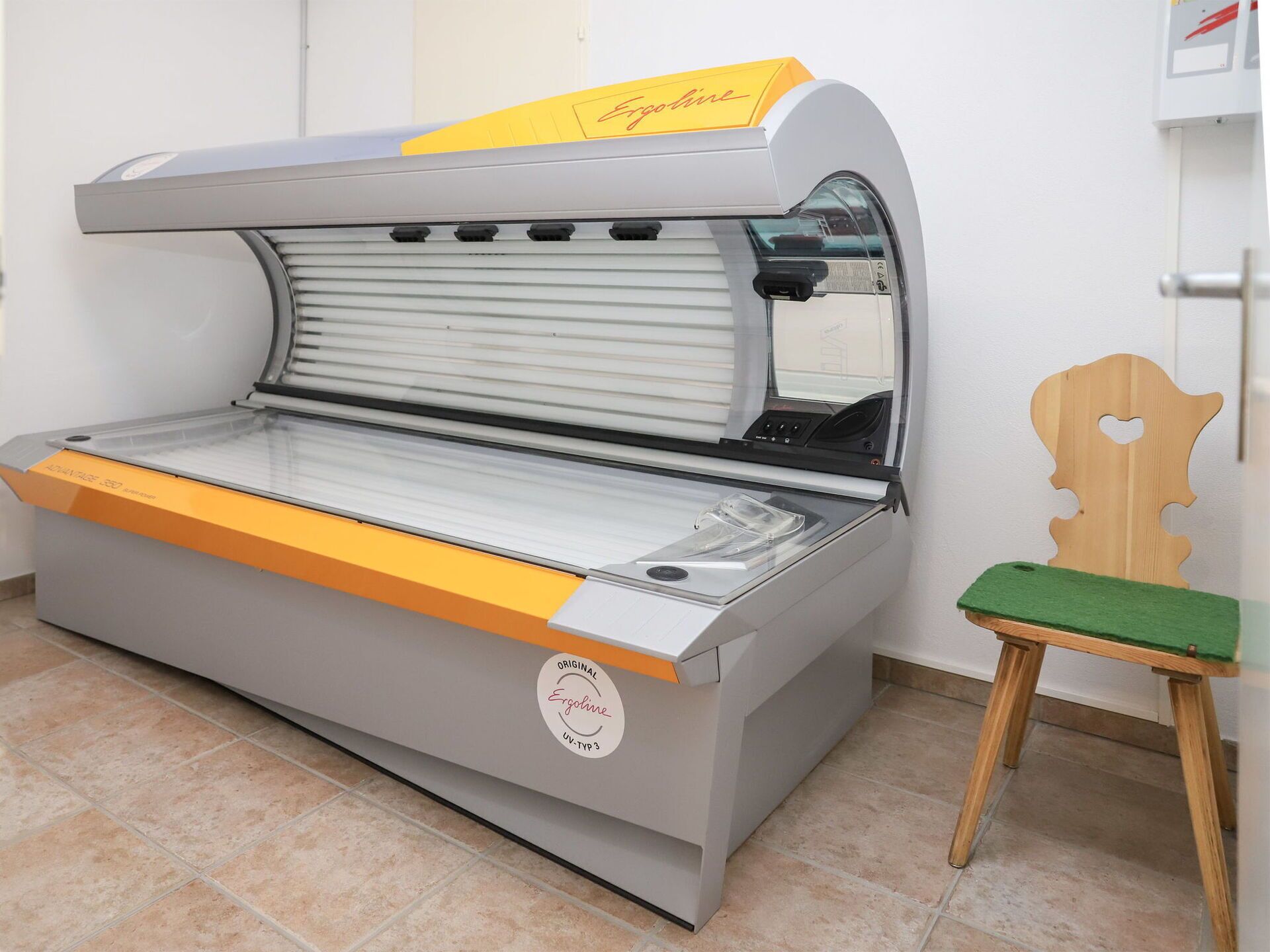 Een medische echografiemachine met een bedieningspaneel, een groene stoel en een houten stoel met een hartvormig uitsparing.