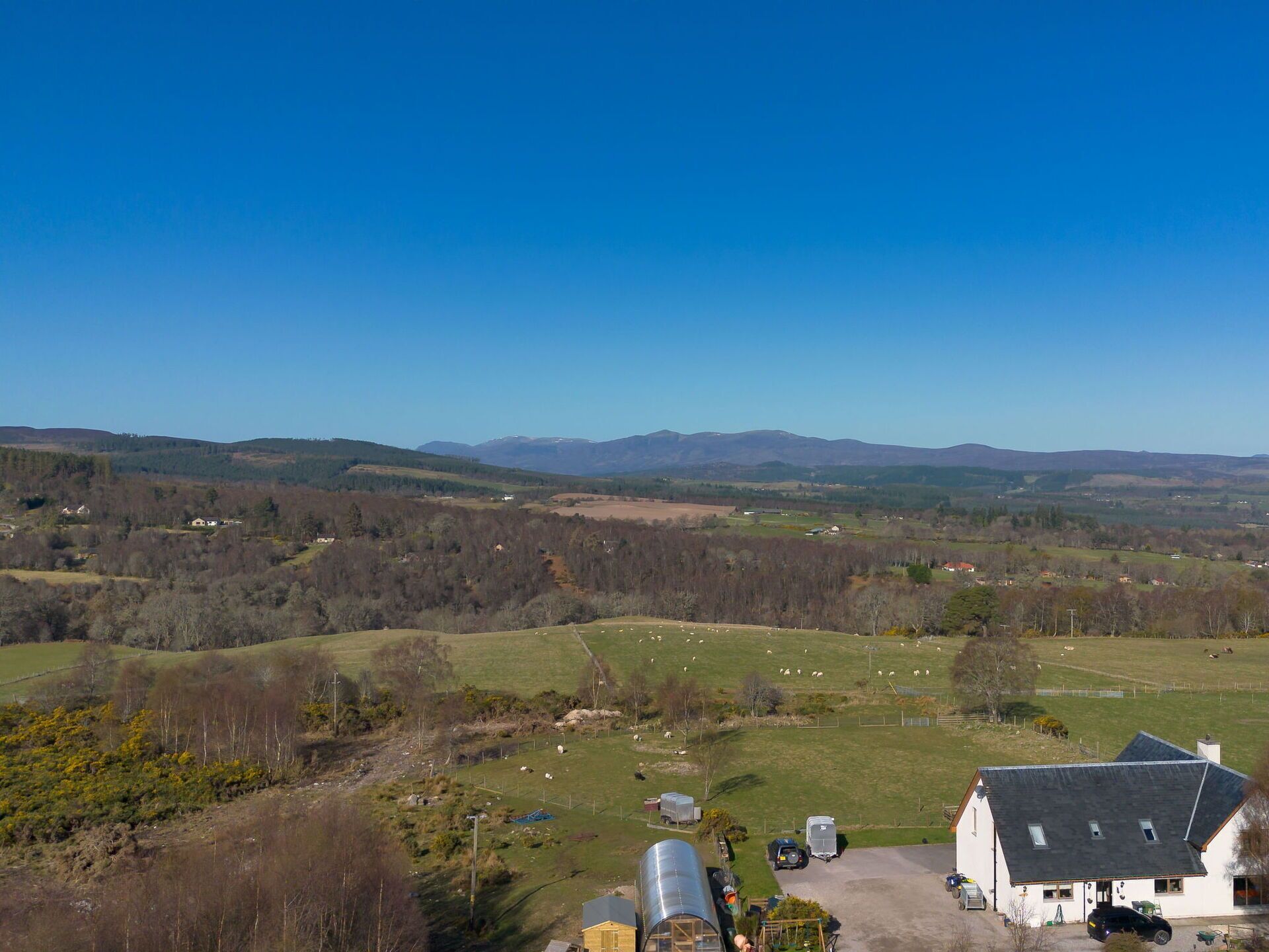 A rural landscape with a farmhouse, open fields, and distant mountains.