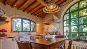 Una cocina rústica con una mesa de madera, sillas y un ventanal con vistas a la vegetación.