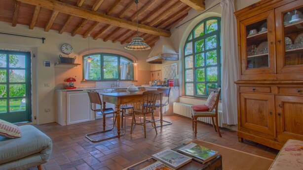 Cocina rústica con vigas de madera, comedor con sillas, un ventanal grande y un mueble con puertas de vidrio.