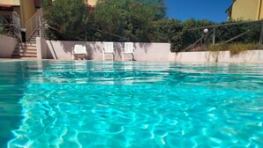 Ein klares, blaues Schwimmbecken mit Stufen, umgeben von weißen Stühlen und viel Grün.