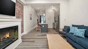 Una sala de estar moderna con chimenea, un televisor montado en la pared, un sofá y una cocina al fondo.