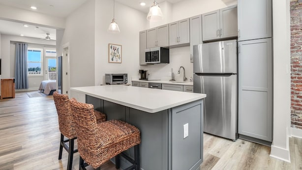 A modern kitchen with grey cabinets, stainless steel appliances, a large island with bar stools, and a view of the living area.