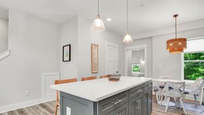 Een moderne keuken met een centraal eiland, hanglampen en een eetgedeelte met witte stoelen.