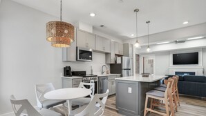 Een moderne keuken met grijze kastjes, een centraal eiland en een eetgedeelte met witte stoelen.
