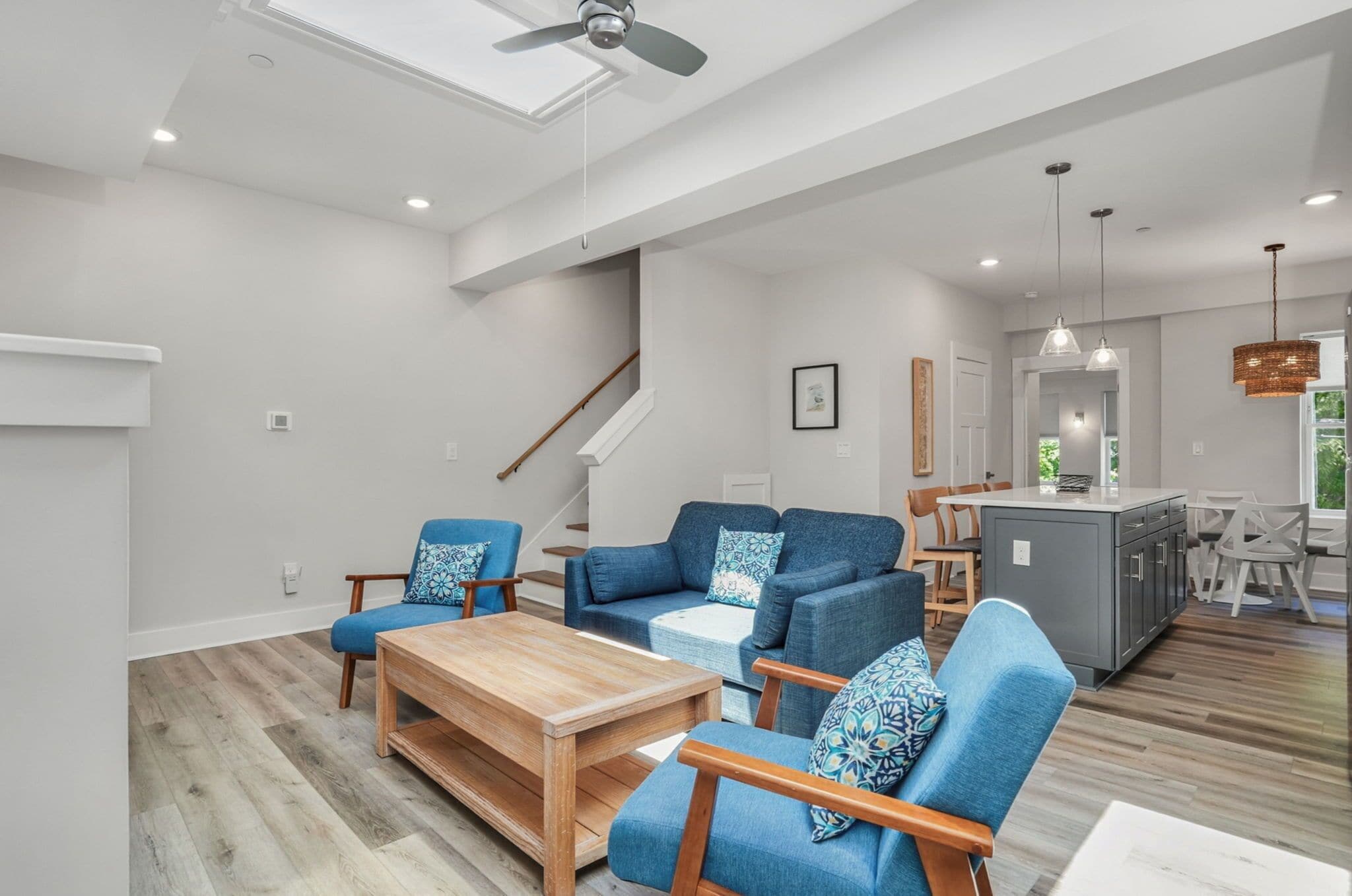 A spacious living area with a wooden coffee table, blue upholstered chairs, and a kitchen island.