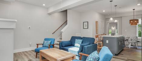 A spacious living area with a wooden coffee table, blue upholstered chairs, and a kitchen island.