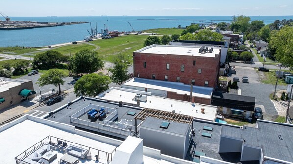 Un edificio de varios pisos con una terraza en la azotea, un edificio de ladrillo con techo plano y una vista al mar y al puerto en el fondo.