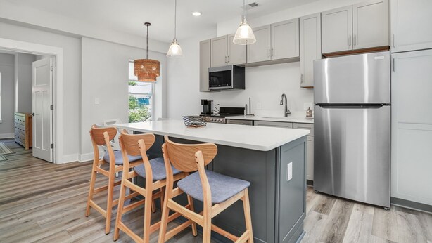 Een moderne keuken met een centraal eiland, roestvrijstalen apparatuur en houten barstoelen.