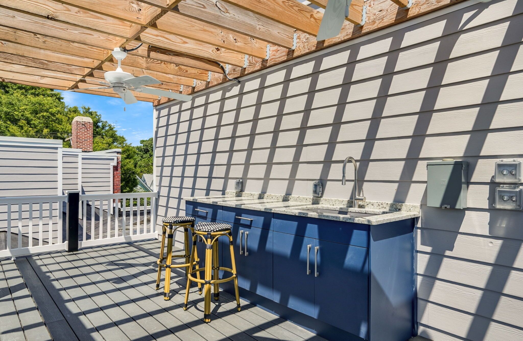 An outdoor kitchen area with a built-in bar, two stools, and a ceiling fan.
