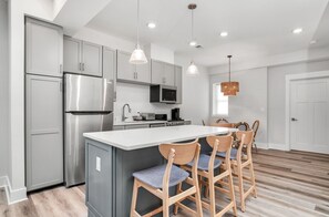 A modern kitchen with grey cabinets, stainless steel appliances, a central island with bar stools, and pendant lighting.