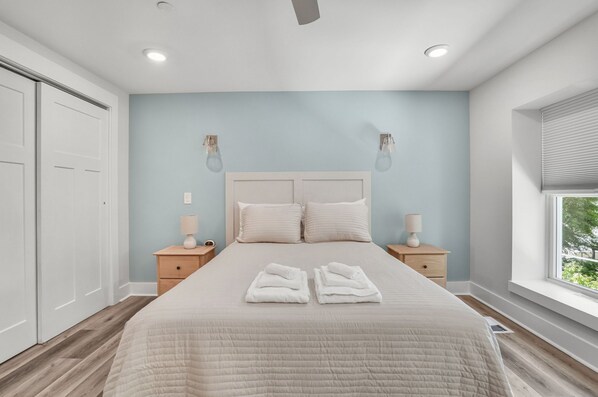 A bedroom with a bed, two bedside tables, a window, and a ceiling fan.