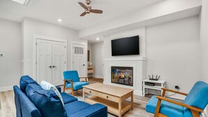 A living room with a sofa, chairs, a coffee table, a fireplace, a TV, and a ceiling fan.