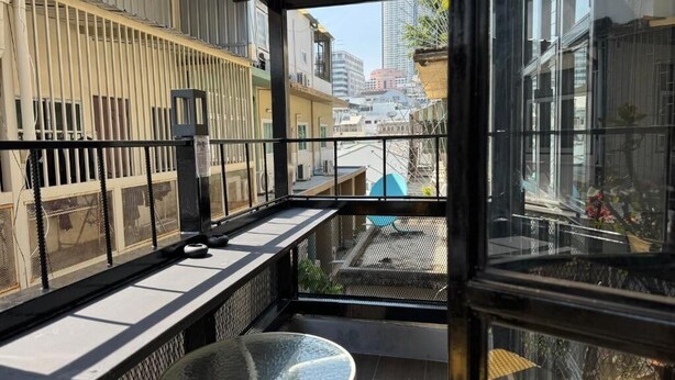 A balcony with a glass table and a metal railing, overlooking a cityscape. - STAY AT PAN (Bangkok)